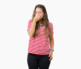 Fototapeta premium Young beautiful brunette woman wearing stripes t-shirt over isolated background smelling something stinky and disgusting, intolerable smell, holding breath with fingers on nose. Bad smells concept.