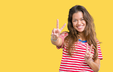 Young beautiful brunette woman wearing stripes t-shirt over isolated background smiling looking to the camera showing fingers doing victory sign. Number two.