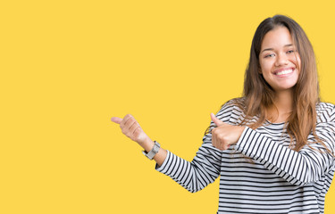 Young beautiful brunette woman wearing stripes sweater over isolated background Pointing to the back behind with hand and thumbs up, smiling confident
