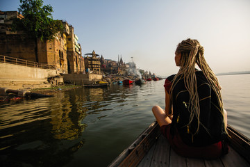 Woman traveler on a boat glides through the water on Ganges river along the shore of Varanasi,...