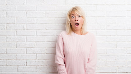 Adult caucasian woman over white brick wall wearing winter sweater afraid and shocked with surprise...