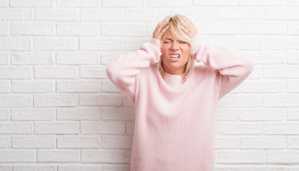 Adult caucasian woman over white brick wall wearing winter sweater suffering from headache desperate and stressed because pain and migraine. Hands on head.