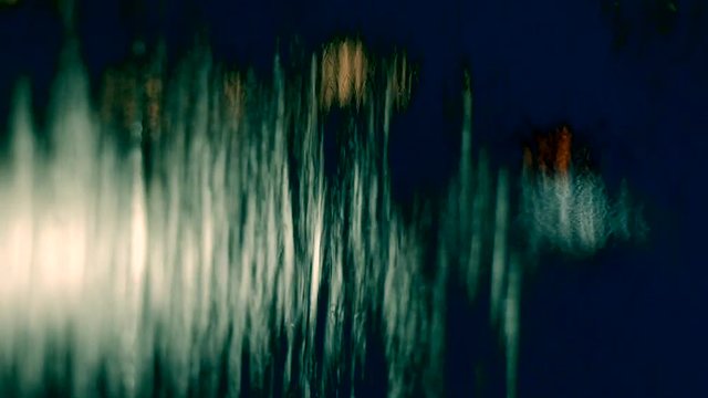HD footage background of water curtain dropping from the wall with blurred focus and bokeh of city light moving on it.