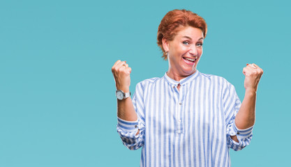 Fototapeta premium Atrractive senior caucasian redhead woman over isolated background celebrating surprised and amazed for success with arms raised and open eyes. Winner concept.