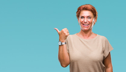 Atrractive senior caucasian redhead woman over isolated background smiling with happy face looking and pointing to the side with thumb up.