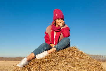 The concept of livestyle  outdoor in autumn. Close up of a young woman student in a warm autumn clothes looking funny, smilling, posing for the camera on  haystick