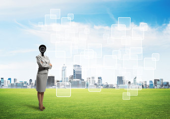 Camera headed woman standing on green grass against modern cityscape