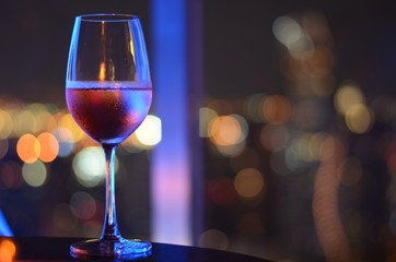 A glass of Rosé wine with bokeh light at Bangkok city and colorful light from rooftop building.