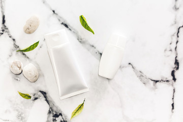 Cosmetic bottle skin care products with spa stones and leaves on white marble background.flat lay