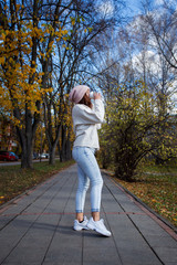 Happy young adult woman walking at beautiful autumn city street drinking coffee to go wearing warm coat and hat