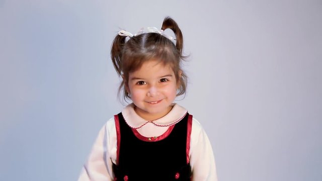 Precocious little girl on plain background makes funny face with tongue out, arms outstretched and rocks back and forth.  Cute smile, silly girl, funny faces.  She has pig tails.
