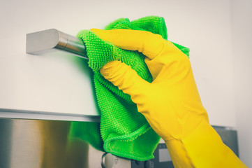 Hand in glove with green rag is cleaning stainless steel handles