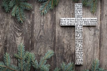 White wooden cross with the Lord's prayer on the shabby dark wooden plank with fir tree branches background