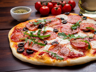 hot homemade Italian pepperoni pizza with salami, mozzarella and olives on a dark brown wooden table