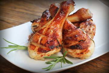 Grilled chicken legs with rosemary served on white plate. Dinner background