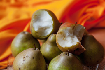 Bitten pears lie on wooden board. Rear orange fabric