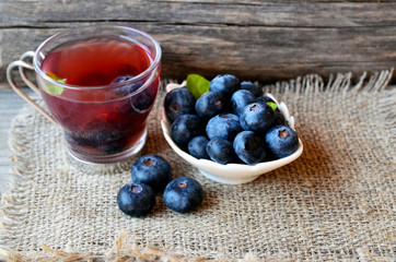 Blueberry tea in a glass cup and fresh blueberries on a burlap cloth on wooden background.Natural herbal beverage.Selective focus.