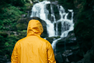 man standing in yellow raincoat and looking at waterfall