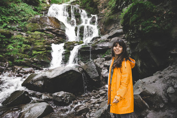 Naklejka premium woman standing in yellow raincoat and looking at waterfall