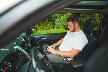 young adult man working in car on laptop