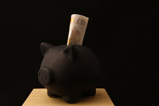Saving money - black piggy banks with 10 pounds on black background with lightings