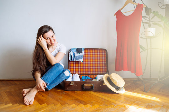 smiling woman sit on floor near valise with clothes. packing bef