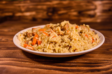 Ceramic plate with pilaf on wooden table