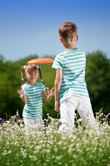 Happy boy and little girl playing with flying disk on a meadow in a sunny day