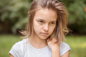 Emotional portrait of attractive caucasian little student girl with beautiful brown eyes in summer city park. Sad or modest child looking away - close-up, outdoors.