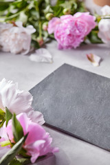 Obraz na płótnie Canvas Slate board decorated with petals and pink flowers of peonies on a gray concrete background with copy space. Flower layout
