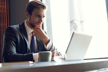 Attractive businessman using a laptop and smiling while working in cafe