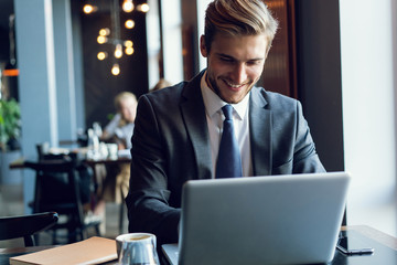 Attractive businessman using a laptop and smiling while working in cafe