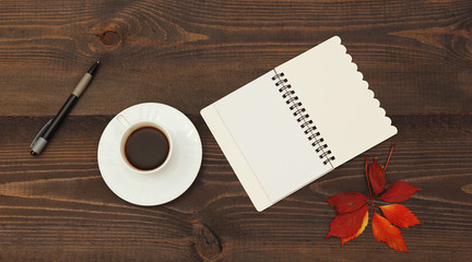 Cup of coffee, open notebook, pen and autumn red leaf on a wooden table. View from above.