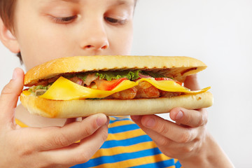 Young cut boy with a tasty cheeseburger on a white background close up