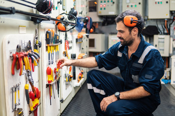 Caucasian marine engineer officer in engine control room ECR. He works in workshop and chooses correct tools and equipment