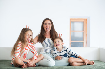 happy mother and two children showing their tongues sitting on sofa indoors fooling around