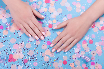 Beautiful young woman's hands on blue pastel background with festive multi color confetti.