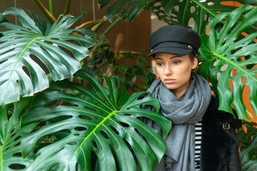 portrait of young woman in hat and scarf posing on background of jungle leaves 
