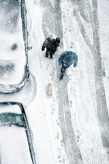 Naklejka na ściany i meble Elevated view of people walking during snow on frozen street with covered parked cars
