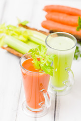 Carrot and celery juice with fresh vegetables on bark plates on wooden background.