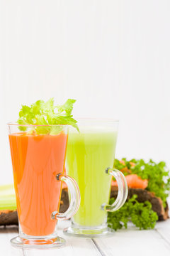 Carrot and celery juice with fresh vegetables on bark plates on wooden background.