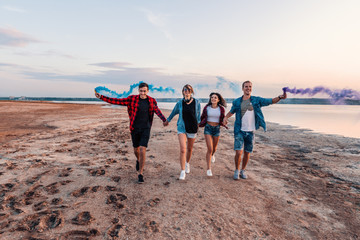 group of young friends running along the beach and holding hand flare or fusee. Freedom and independence concept