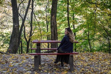 Naklejka na ściany i meble Young beautiful girl sitting on a bench at a table in the autumn park