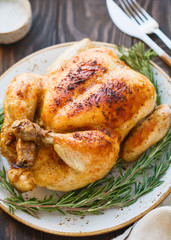 Whole grill chicken with caramelized skin and fresh rosemary on a wooden dinner table.