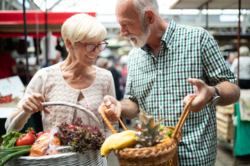 Smiling senior couple holding basket with vegetables at the market