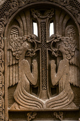 Fototapeta na wymiar Two praying angels near the cross with intertwining ornament,engraved on dark volcanic stone
