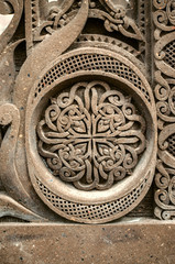 Dark gray volcanic stone with a round ornament of intertwining strips forming a pattern and framed above and below by semicircles with a relief grid



