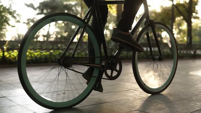 Male faceless legs walking by bicycle on paved road close up side view active lifestyle. Man boy goes with a black coloured bike on street or green park. Healthy life summer outdoor activities. Slow