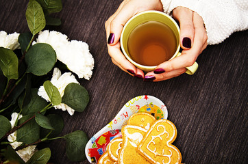 hot green tea in women's hands, flowers and ginger cookies for Christmas