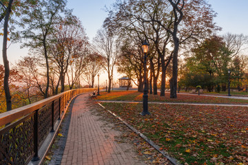 Fototapeta na wymiar Alley with fence, benches and street lights in autumn park